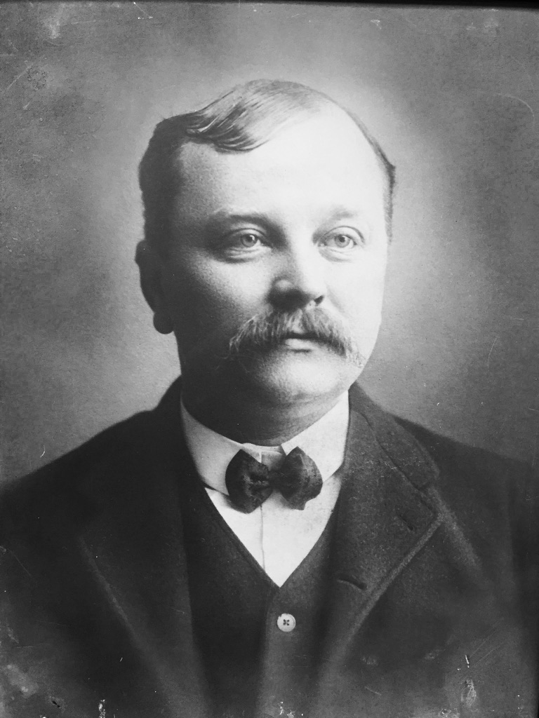A black and white photo of a man with a mustache and a bowtie