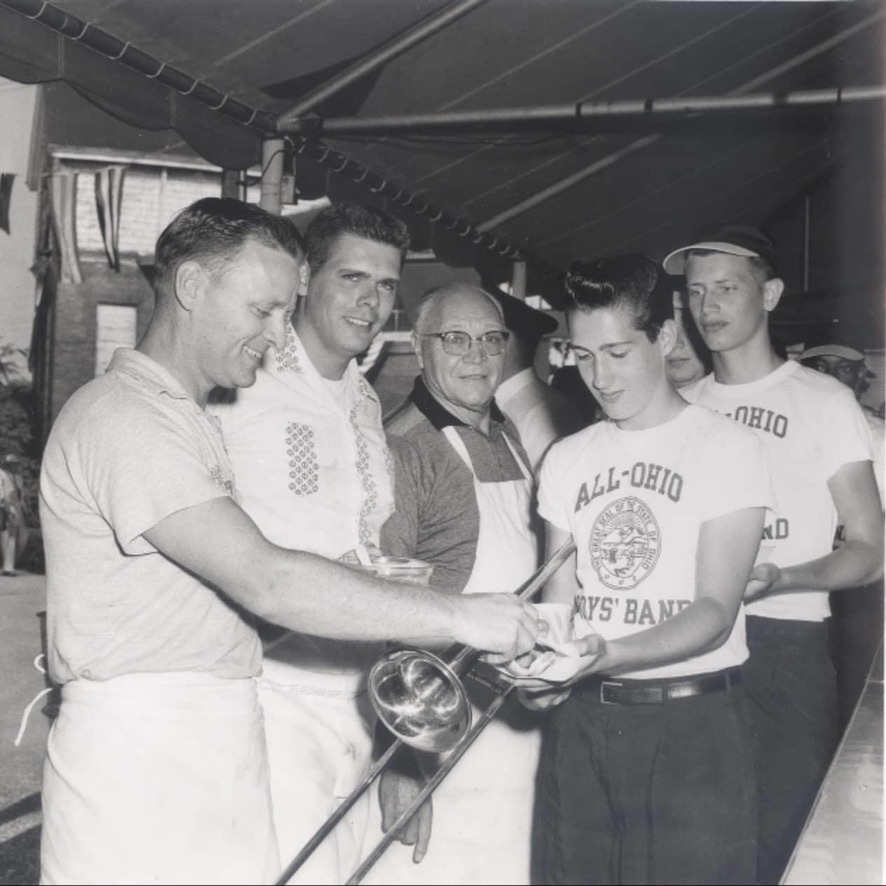 A black and white photo of men in a tent serving hotdogs to other men in the tent