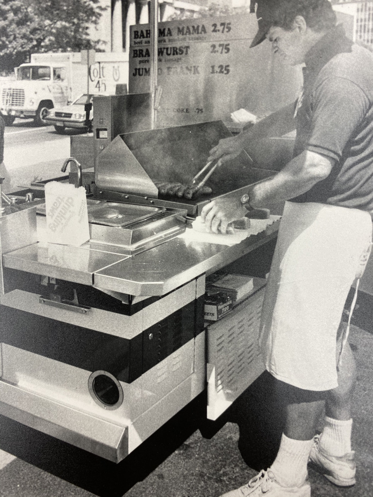 A black and white photo of a man working a food cart